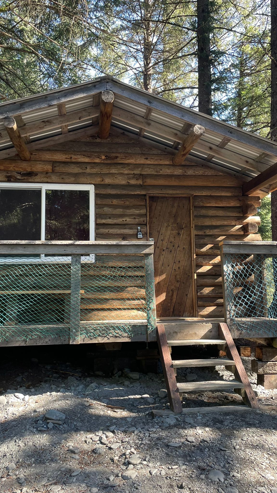 Wooden cabin with a metal roof, porch, and steps in a forest setting.