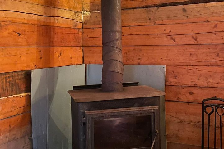Wood stove with chimney in a rustic wooden room, logs stacked nearby.