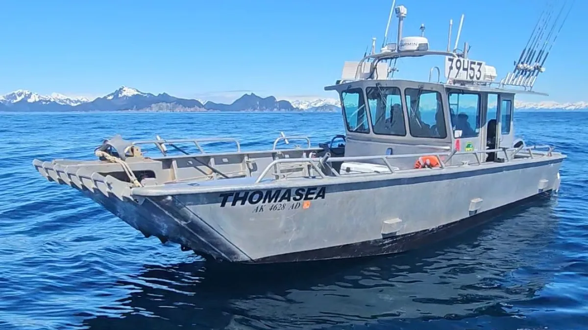 Fishing boat on blue ocean with a rod overhead; snowy mountains in the background.