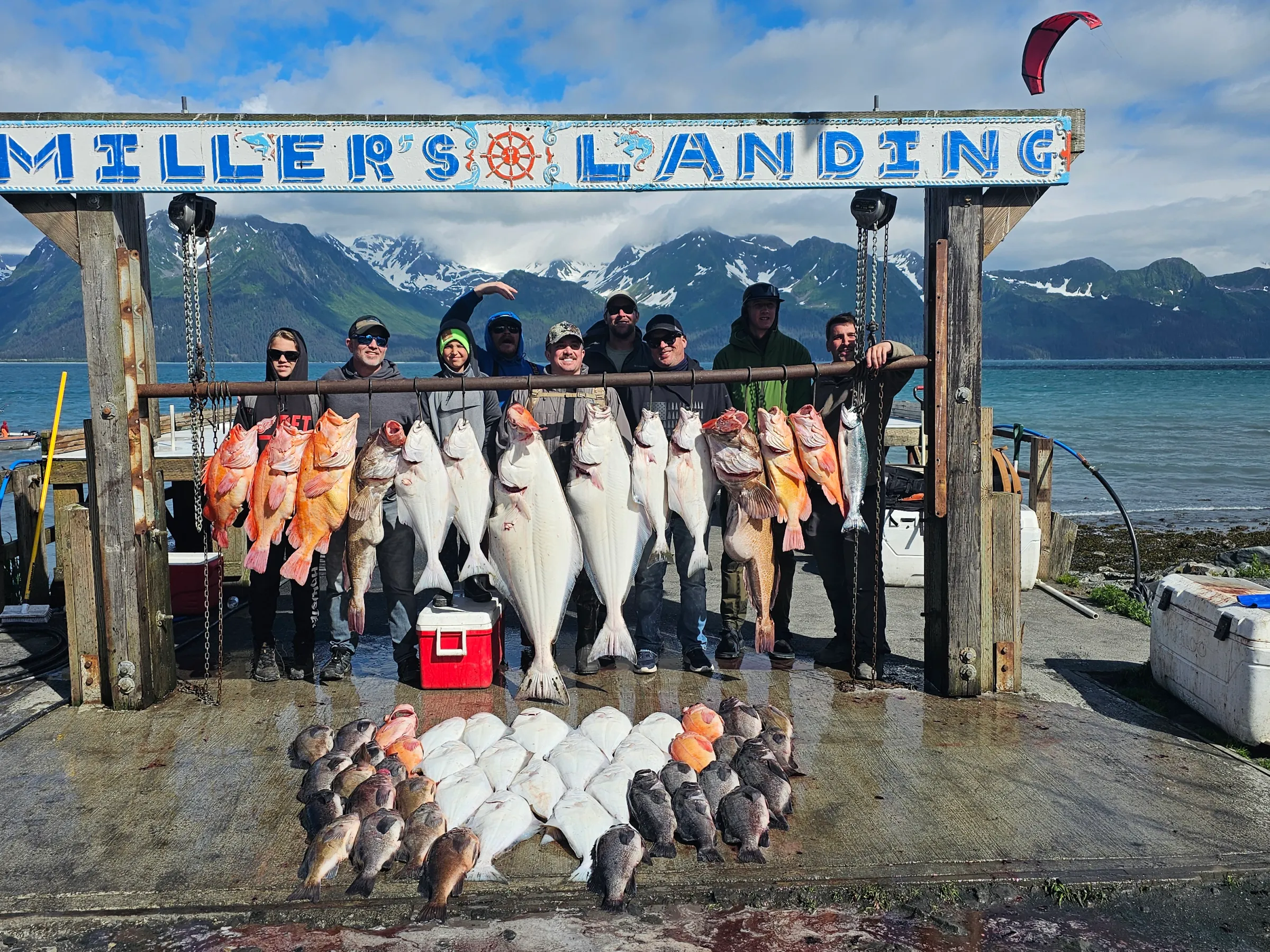 Group holding large fish catch at Miller's Landing, with ocean and mountains in the background.