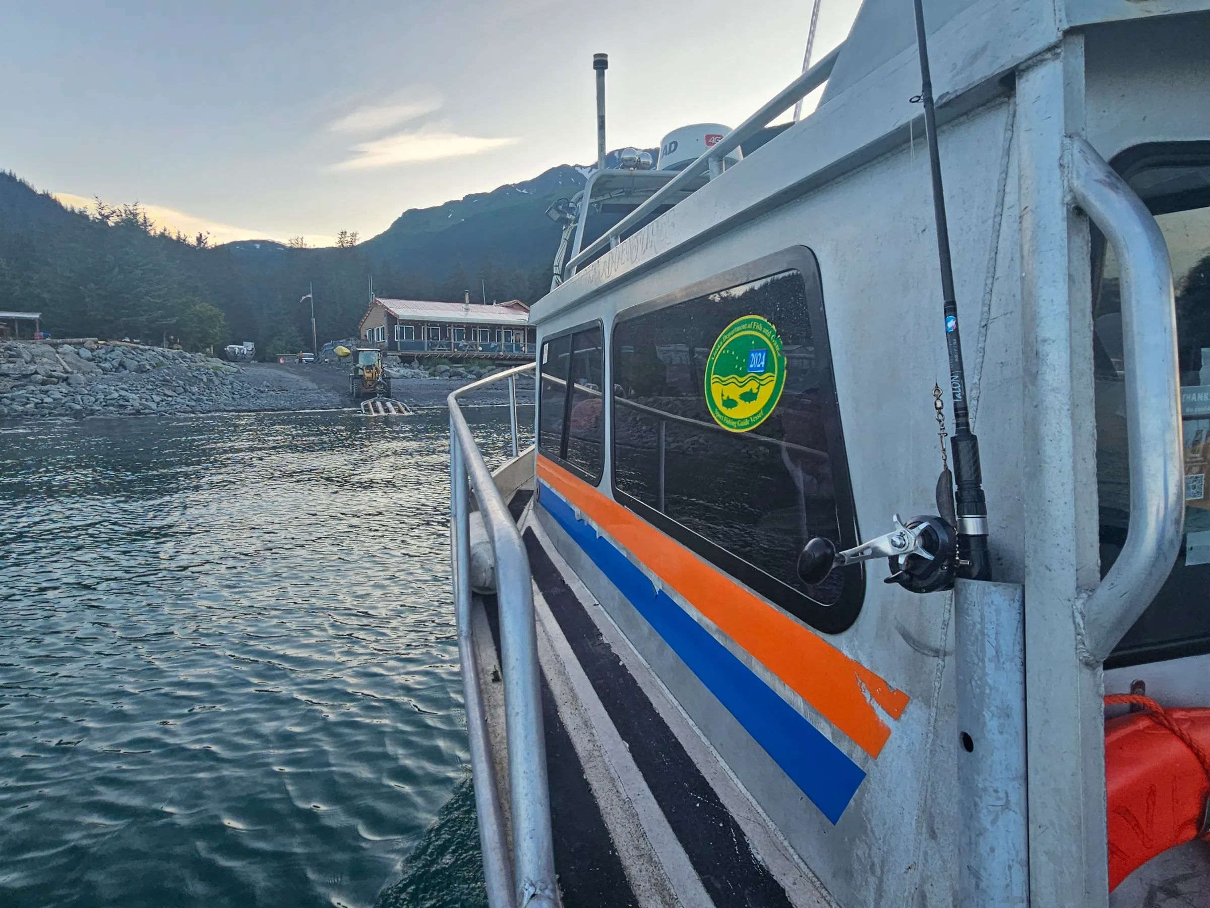 Boat with colorful stripes docked near a rocky shore under a cloudy sky.