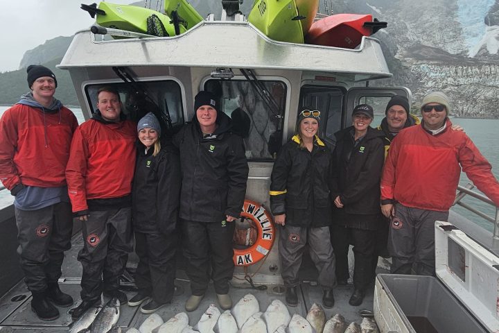 Group of people on a fishing boat with a large catch of fish on the deck.
