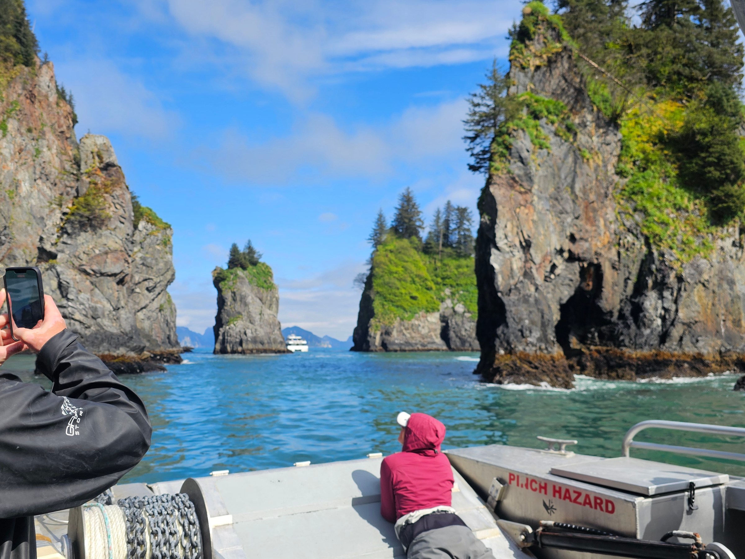 People on a boat taking photos of tall rocky islands in blue water under a clear sky.