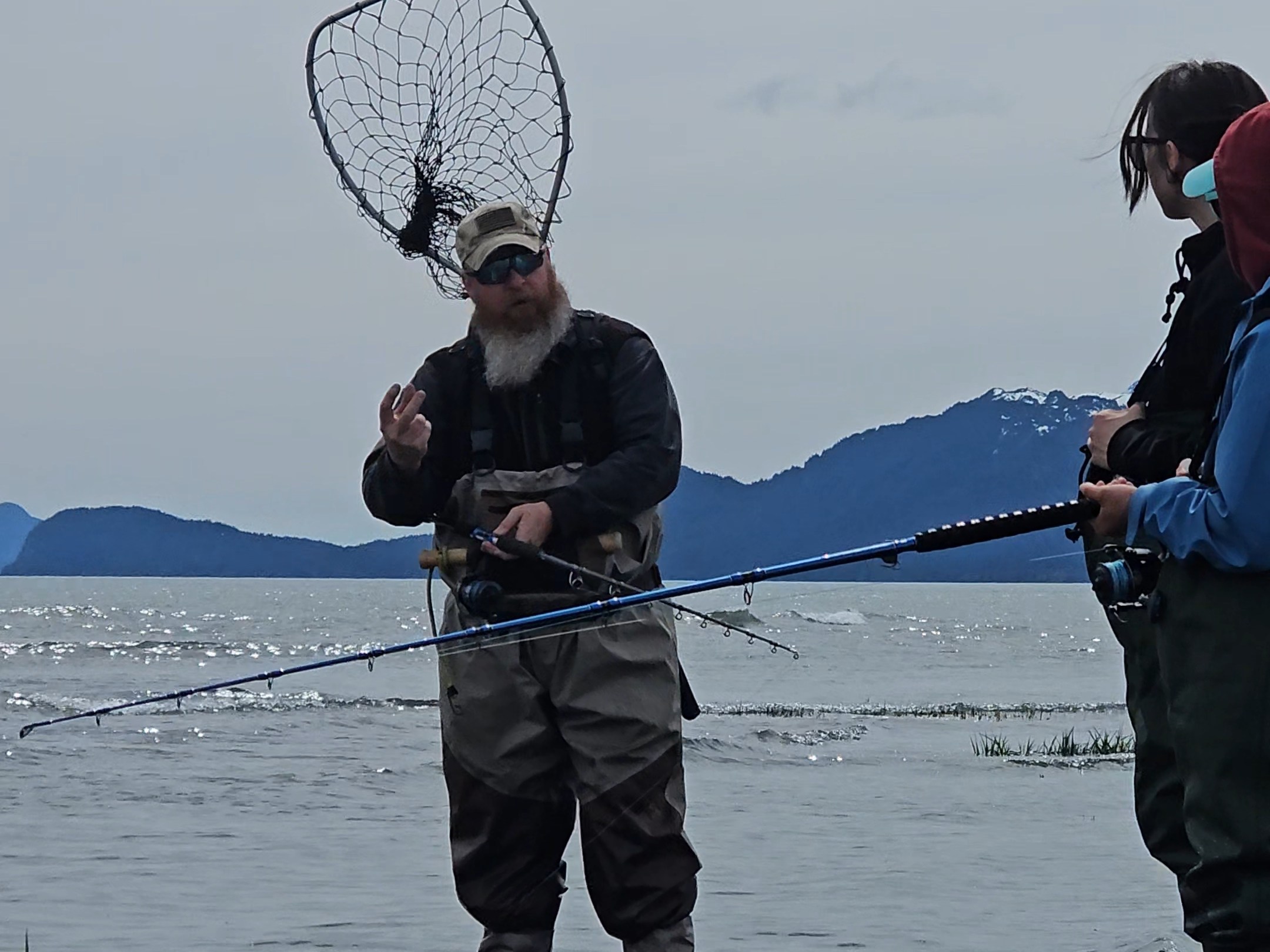 Three people fishing in shallow water with mountains in the background.