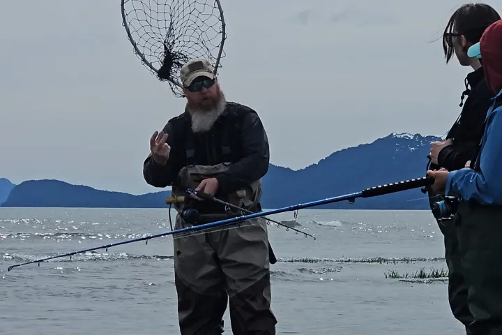 Three people fishing in shallow water with mountains in the background.
