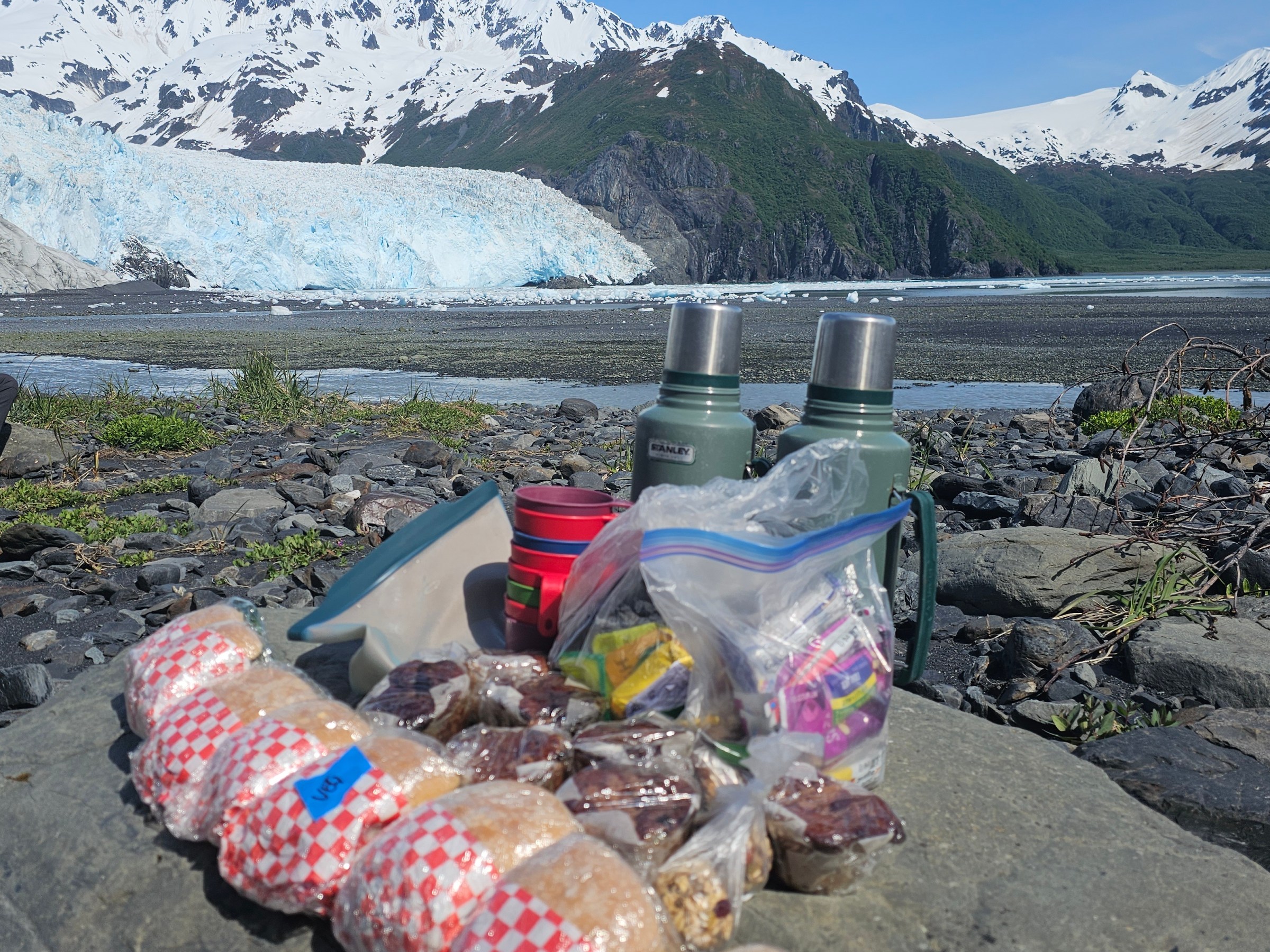 Picnic with sandwiches and thermoses on rocks by glacier and mountains.