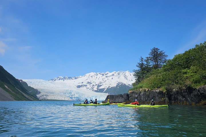 Kayakers on a lake with mountains and a glacier in the background under a clear blue sky.