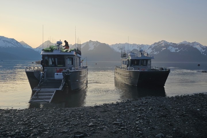 Two boats on a pebbled shore with snow-capped mountains in the background at sunrise.