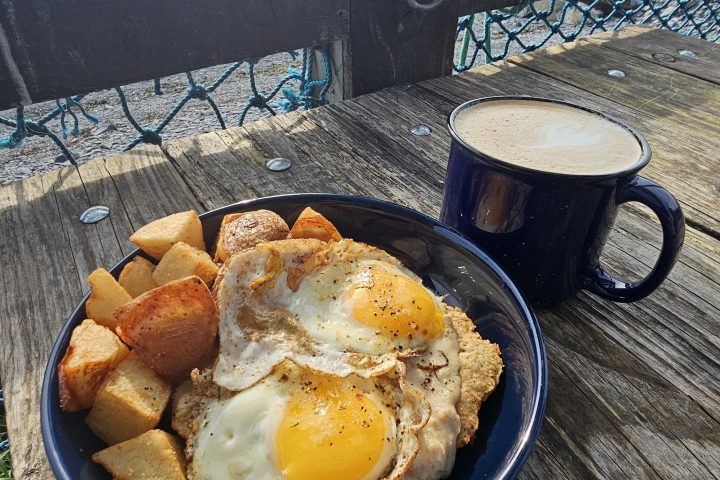 Plate of eggs and potatoes with coffee on a wooden table overlooking a mountain lake.