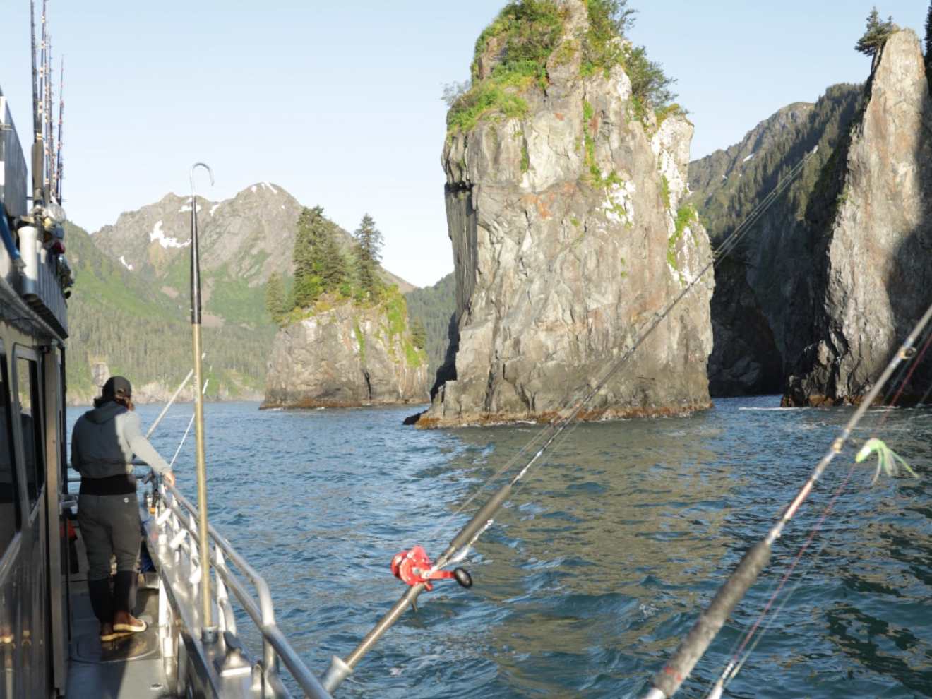 Person on a boat fishing near tall rocky cliffs in a scenic coastal area.