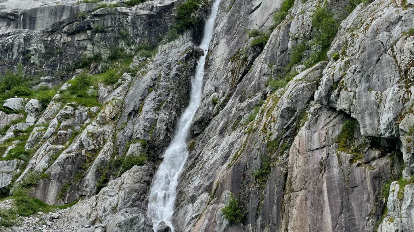 Two kayaks on turquoise water near a waterfall cascading down a rocky cliff.