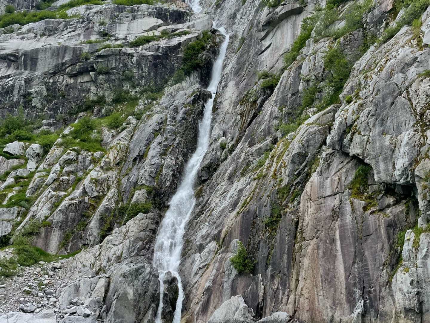 Two kayaks on turquoise water near a waterfall cascading down a rocky cliff.