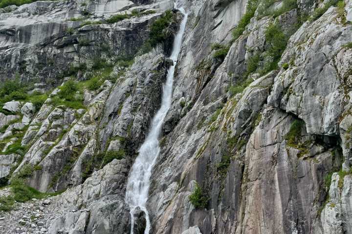 Two kayaks on turquoise water near a waterfall cascading down a rocky cliff.