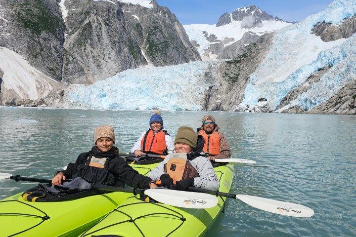 Four people kayaking near a glacier in a mountainous area on a sunny day.
