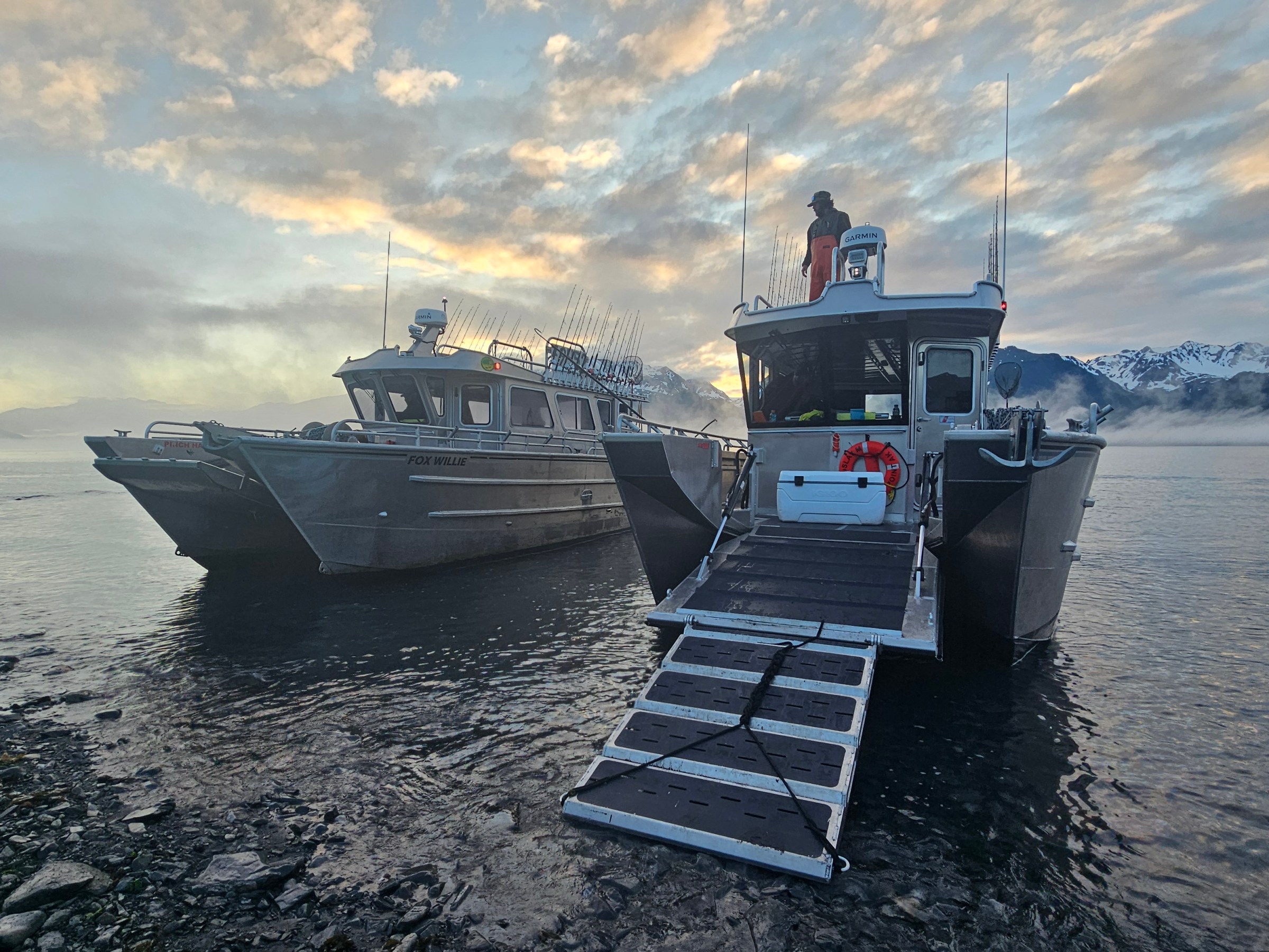 Two fishing boats on a misty lake with mountains and cloudy sky in the background.