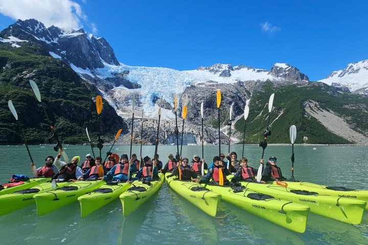 Group of kayakers in yellow kayaks on a lake with a glacier and mountains in the background.