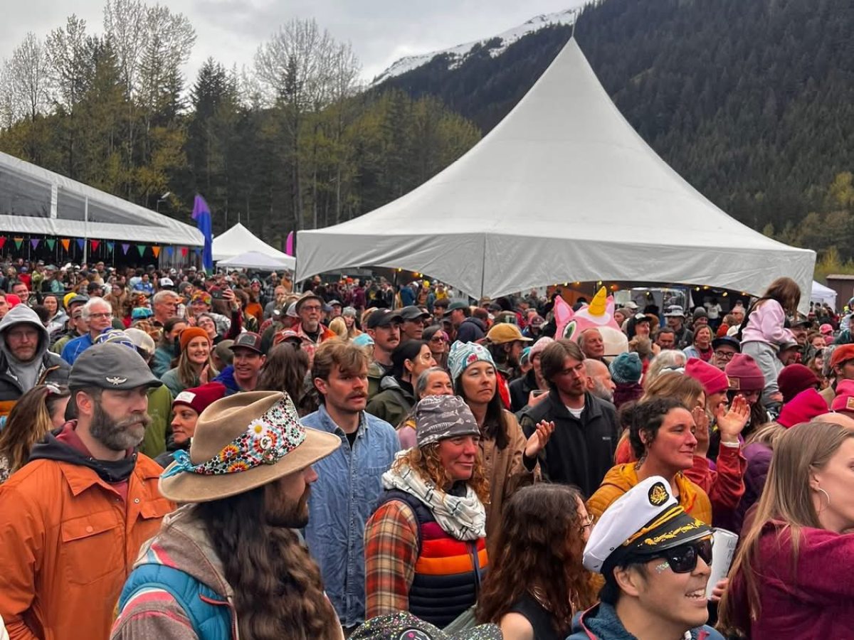 Outdoor festival crowd near tents and mountains under a cloudy sky.