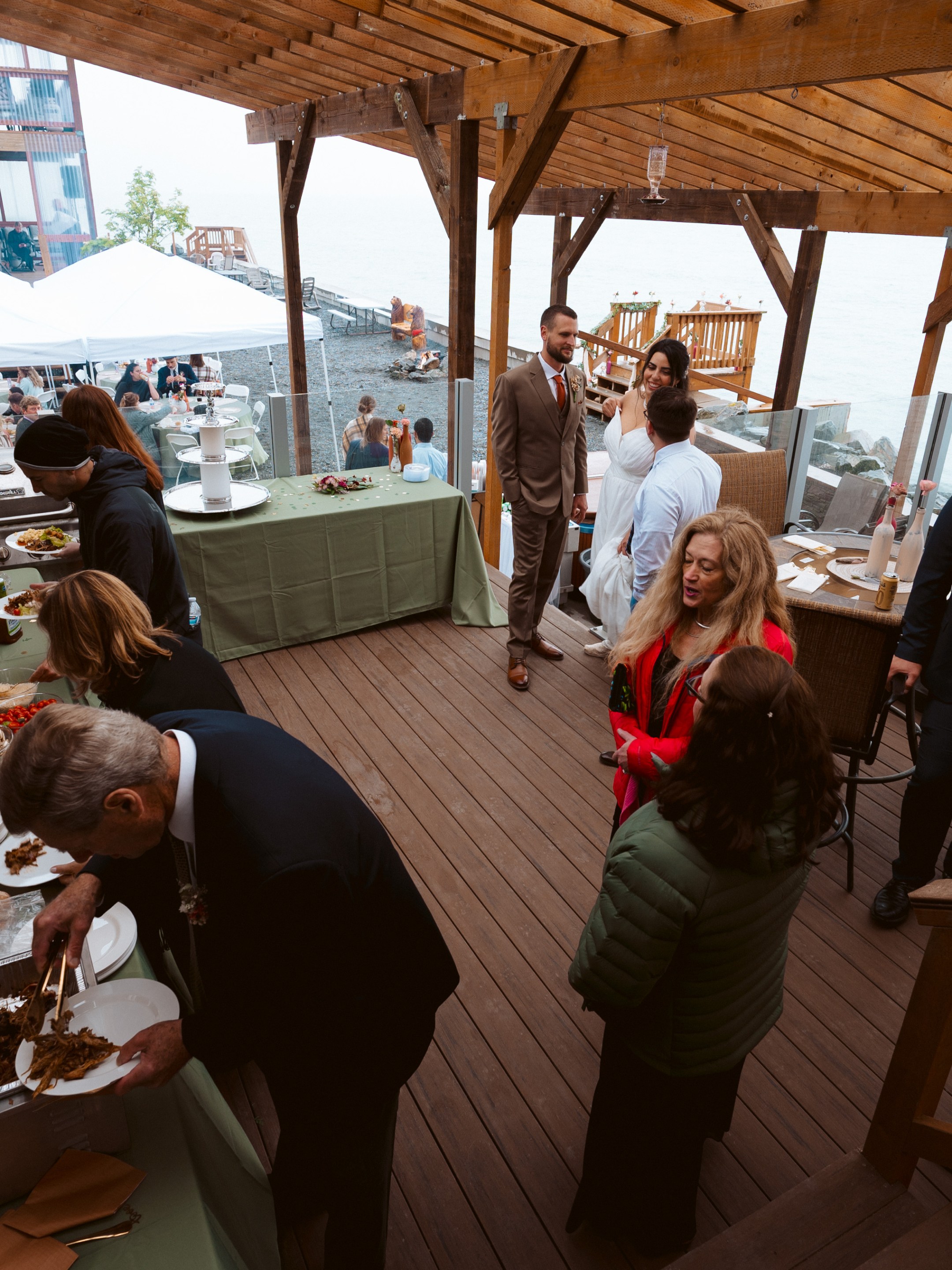 People at an outdoor buffet event on a wooden deck by the water.