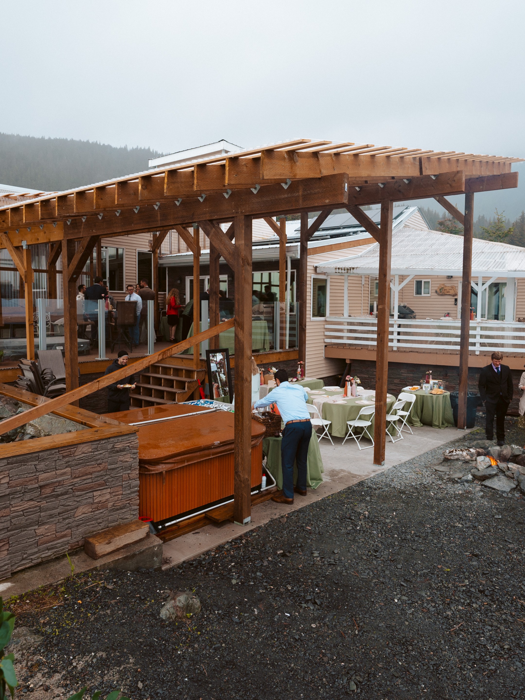 Outdoor gathering with tables, pavilion, and mountain backdrop on a cloudy day.