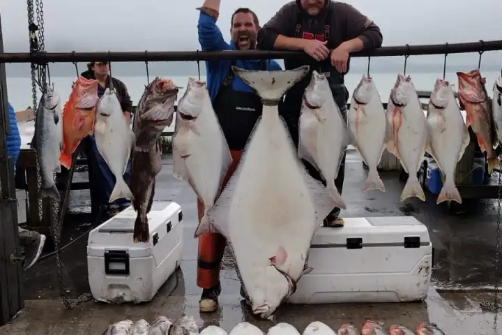 Two people with hanging fish under a sign, fish laid out on wet ground below.