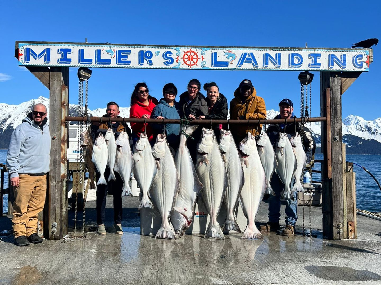 Group with fish catch at Miller's Landing, snowy mountains in background under clear blue sky.