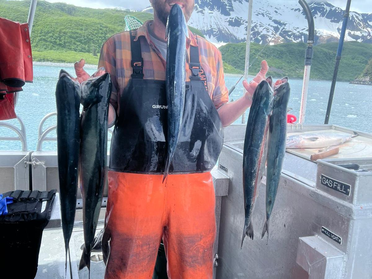 Person in orange overalls holding fish on a boat with mountains in the background.