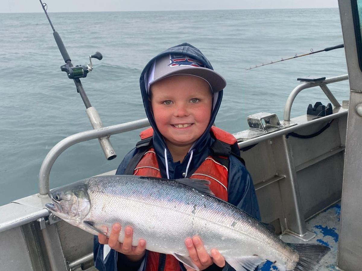 Child on a boat holding a large fish, wearing a lifejacket and hat.