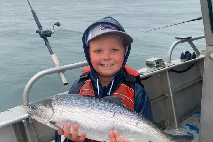 Child on a boat holding a large fish, wearing a lifejacket and hat.