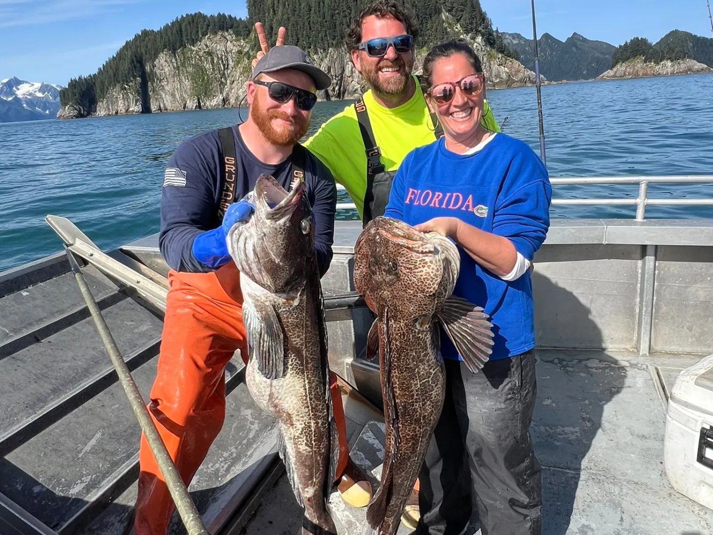 Three people on a boat holding large fish with an island and ocean in the background.