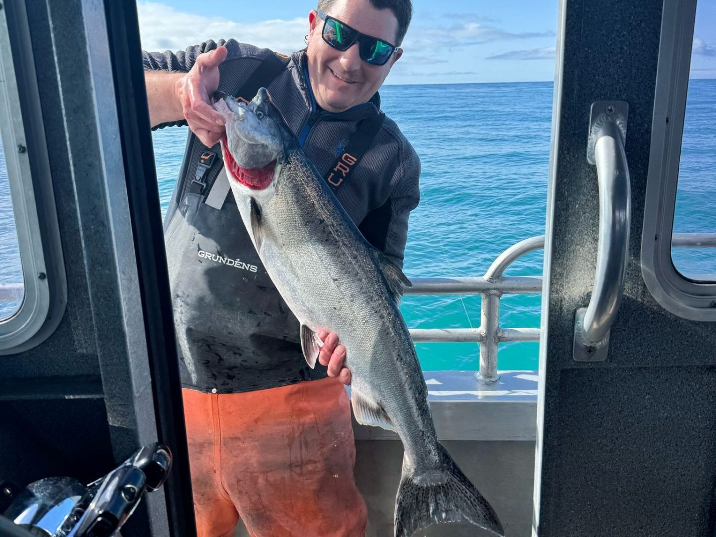 Person holding a large fish on a boat on a sunny day.