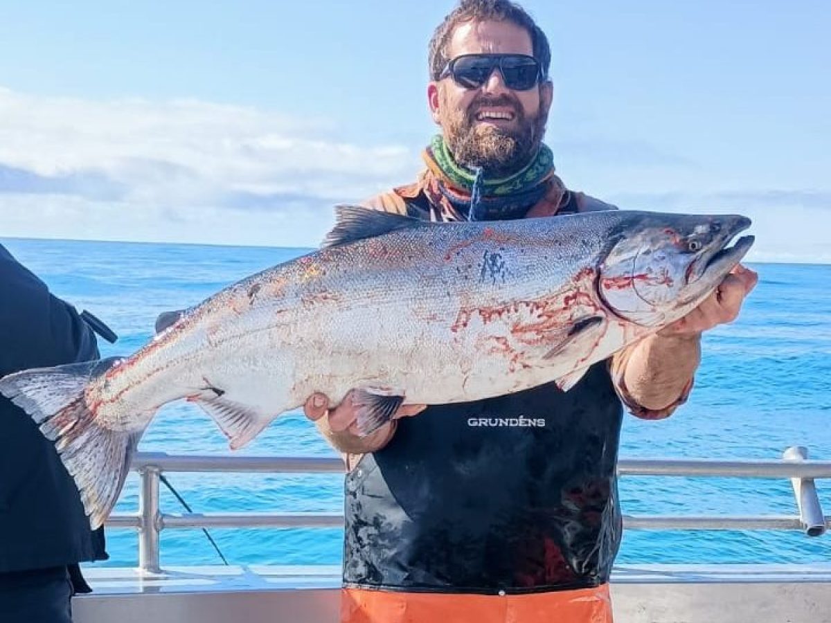 Person in orange gear holding a large fish on a boat with blue ocean background.