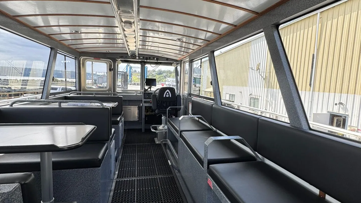 Interior of a boat with benches and tables, showing a view towards the helm.