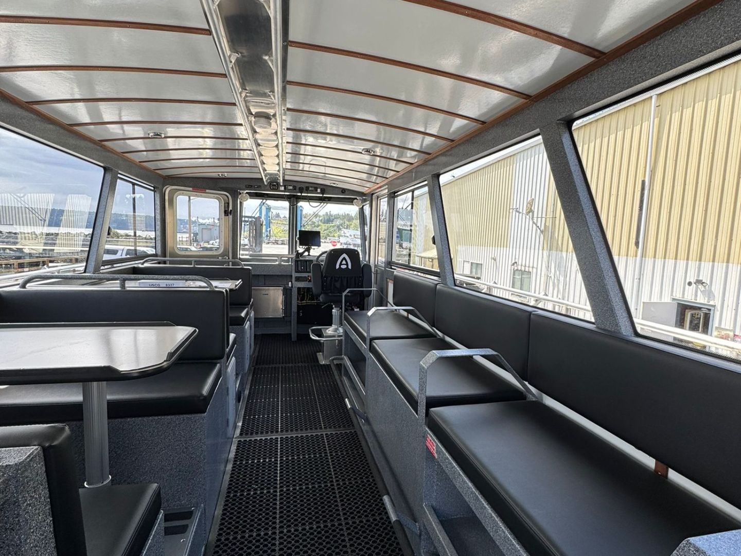 Interior of a boat with benches and tables, showing a view towards the helm.