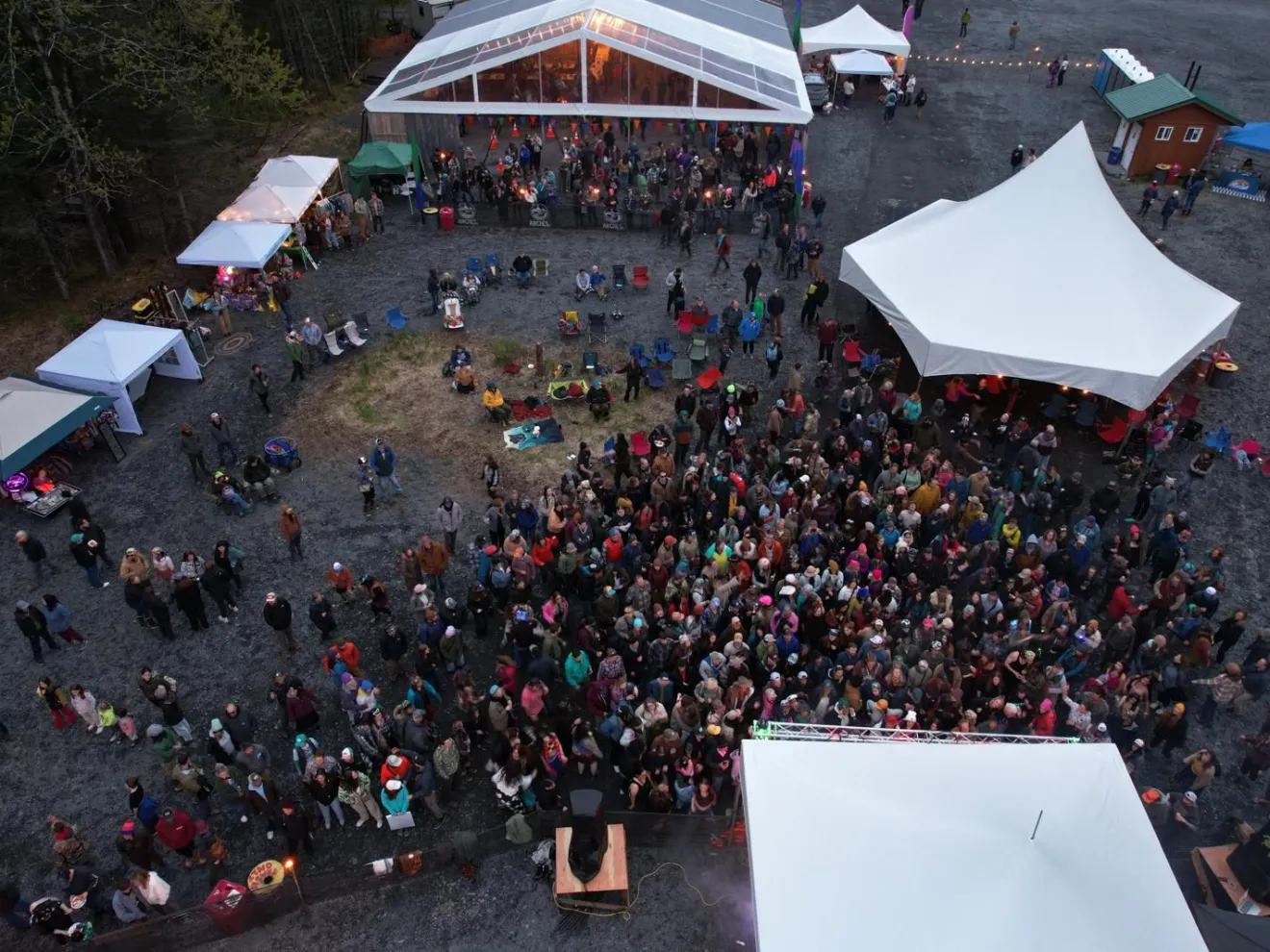 Aerial view of a crowd at an outdoor event with tents and a clear-roofed structure.