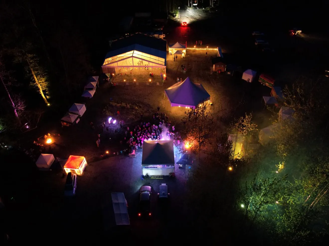 Aerial view of an outdoor night festival with illuminated tents and crowd.