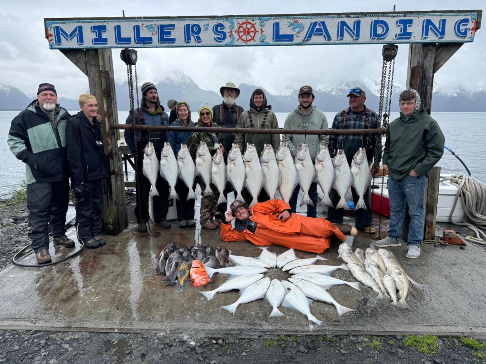 Group of people with large fish catch displayed at 'Miller's Landing' by a lake.