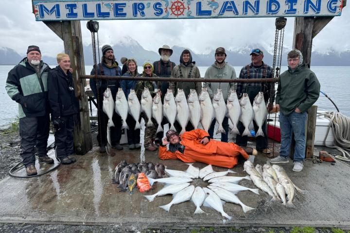 Group of people with large fish catch displayed at 'Miller's Landing' by a lake.