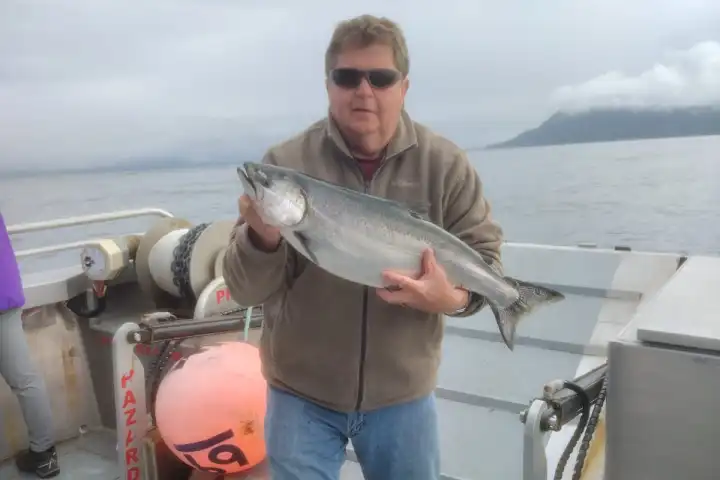 Person on a boat holding a large fish, with cloudy sky and distant mountains in the background.
