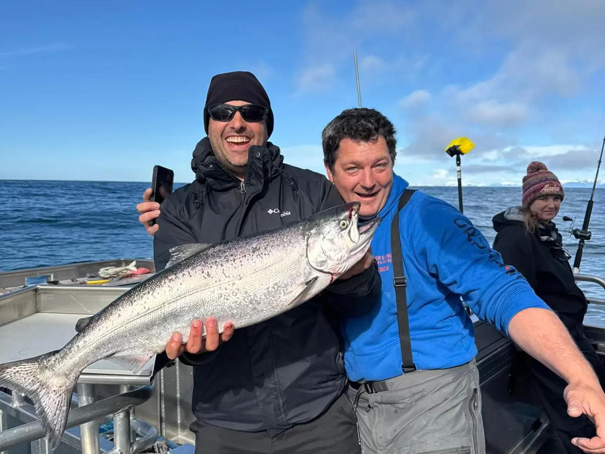 Two men on a boat holding a large fish, with the ocean and blue sky in the background.