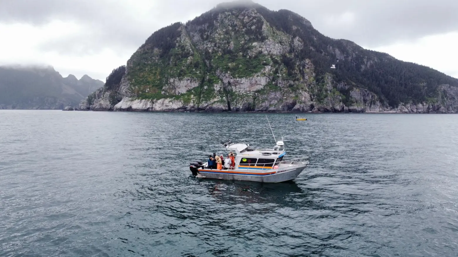 A small boat floats near a rocky, forested island under an overcast sky.