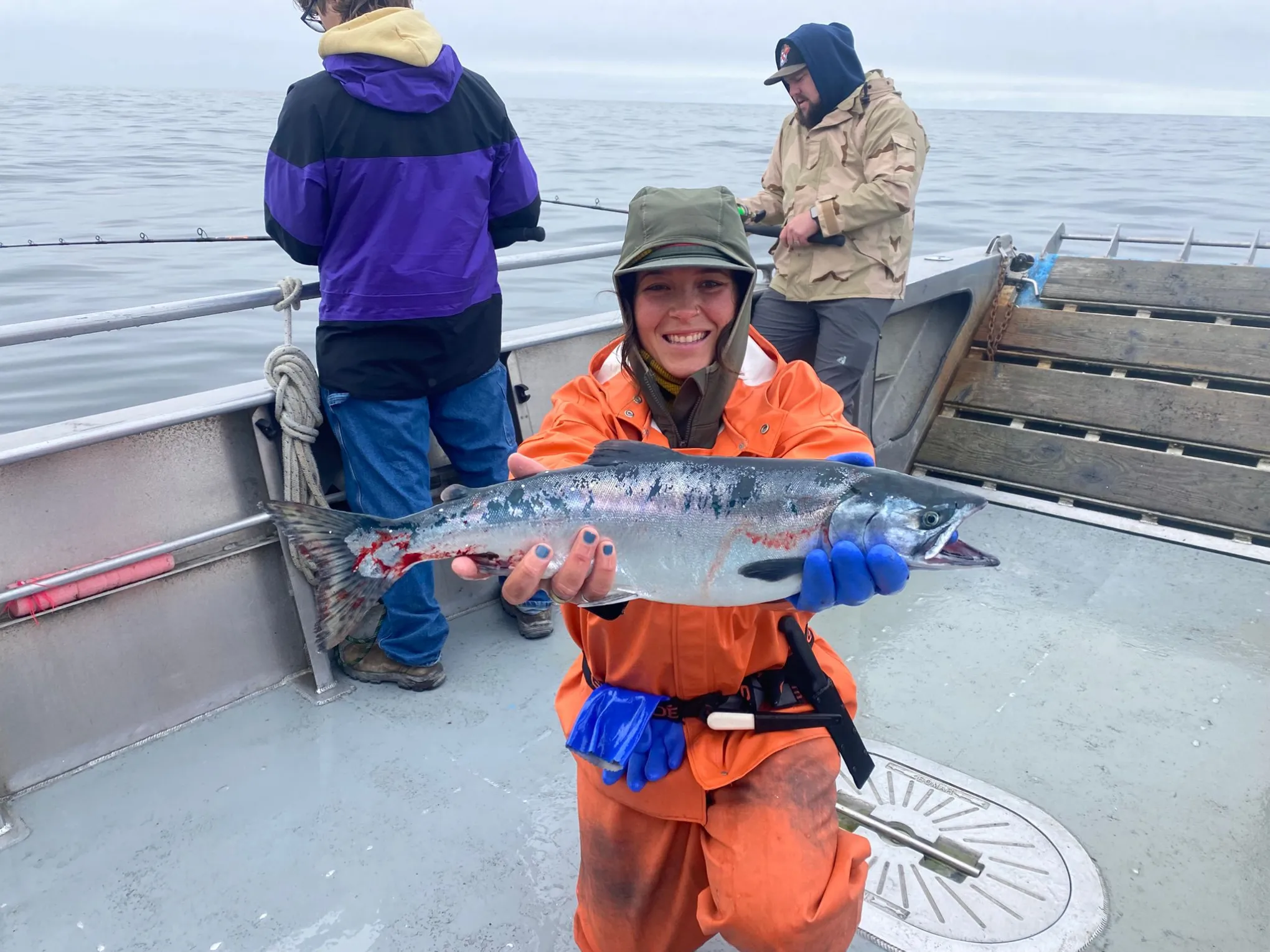 Person in orange jacket holding a fish on a boat, with two others in the background.