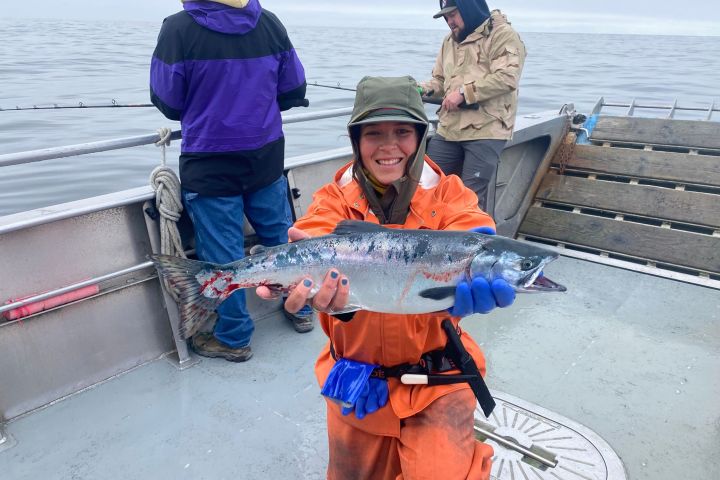 Person in orange jacket holding a fish on a boat, with two others in the background.
