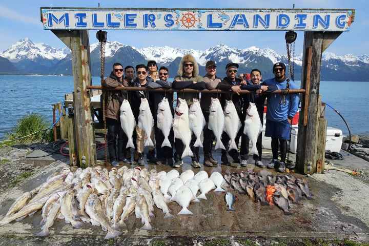 Group of people holding large fish at Miller's Landing with mountains and water in the background.