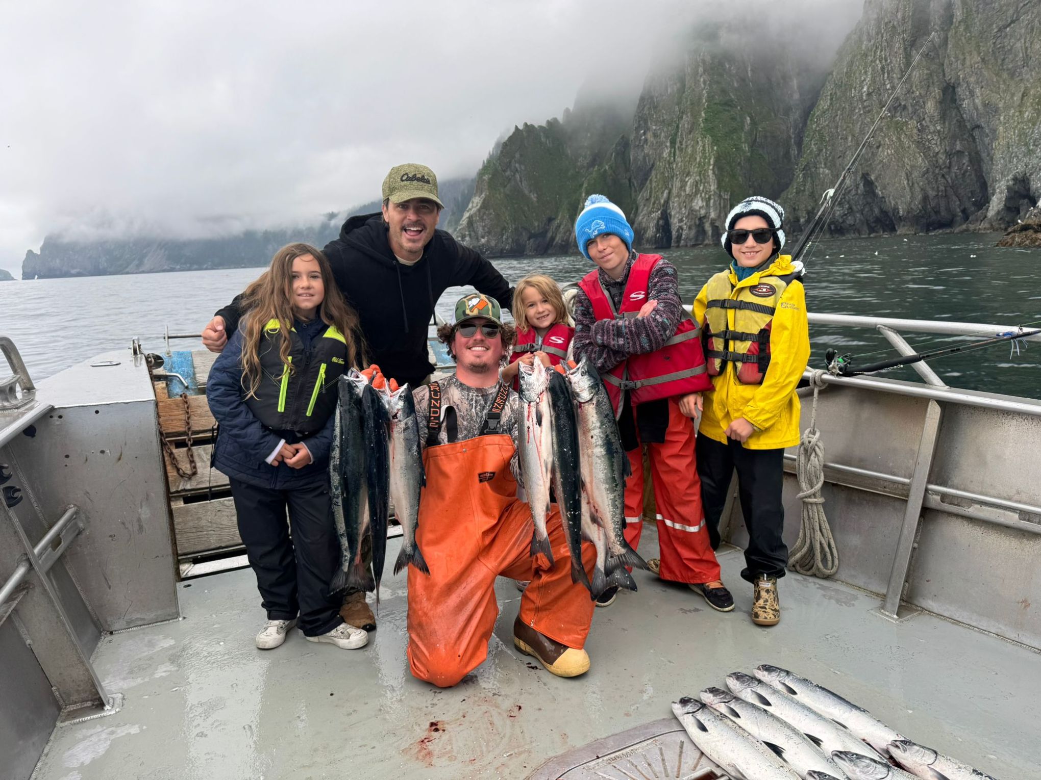 Group of people on a boat holding freshly caught fish with mountains in the background.