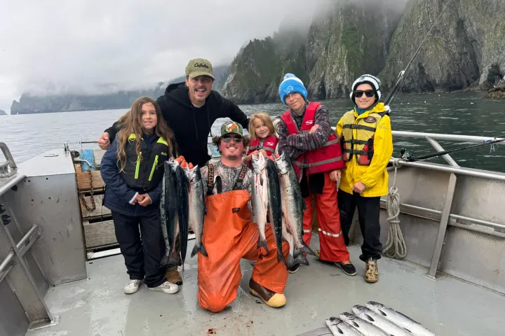 Group of people on a boat holding freshly caught fish with mountains in the background.