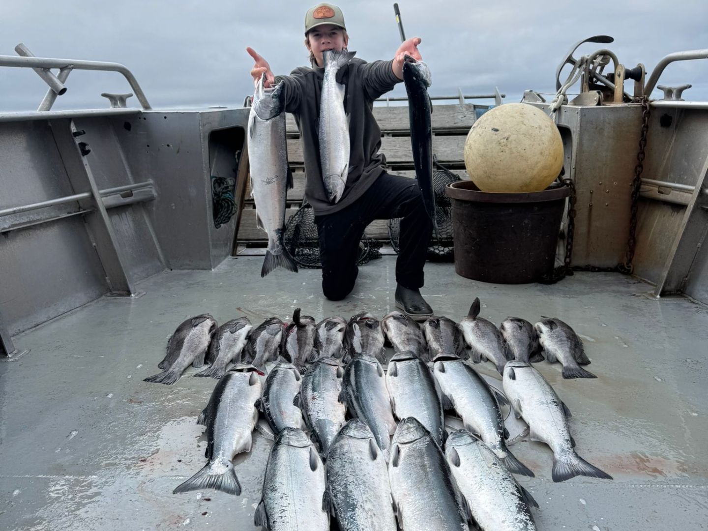 Person kneeling on a boat with numerous fish laid out in front, holding a fish in each hand.