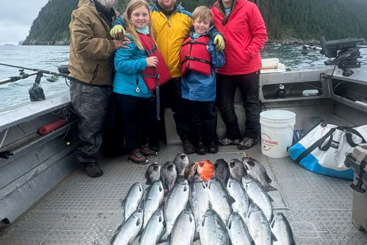Family on boat with caught fish, smiling with mountain and water backdrop.