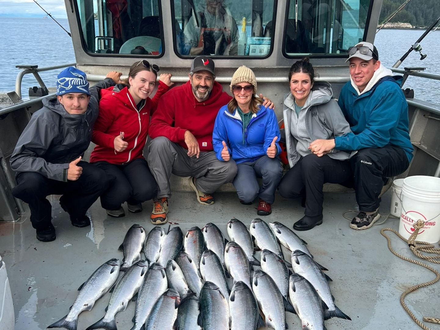 Six people on a boat with freshly caught fish arranged on the deck.