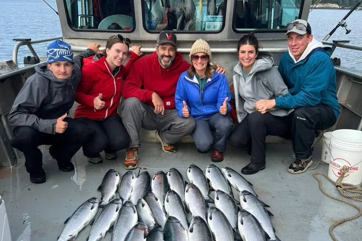 Six people on a boat with freshly caught fish arranged on the deck.
