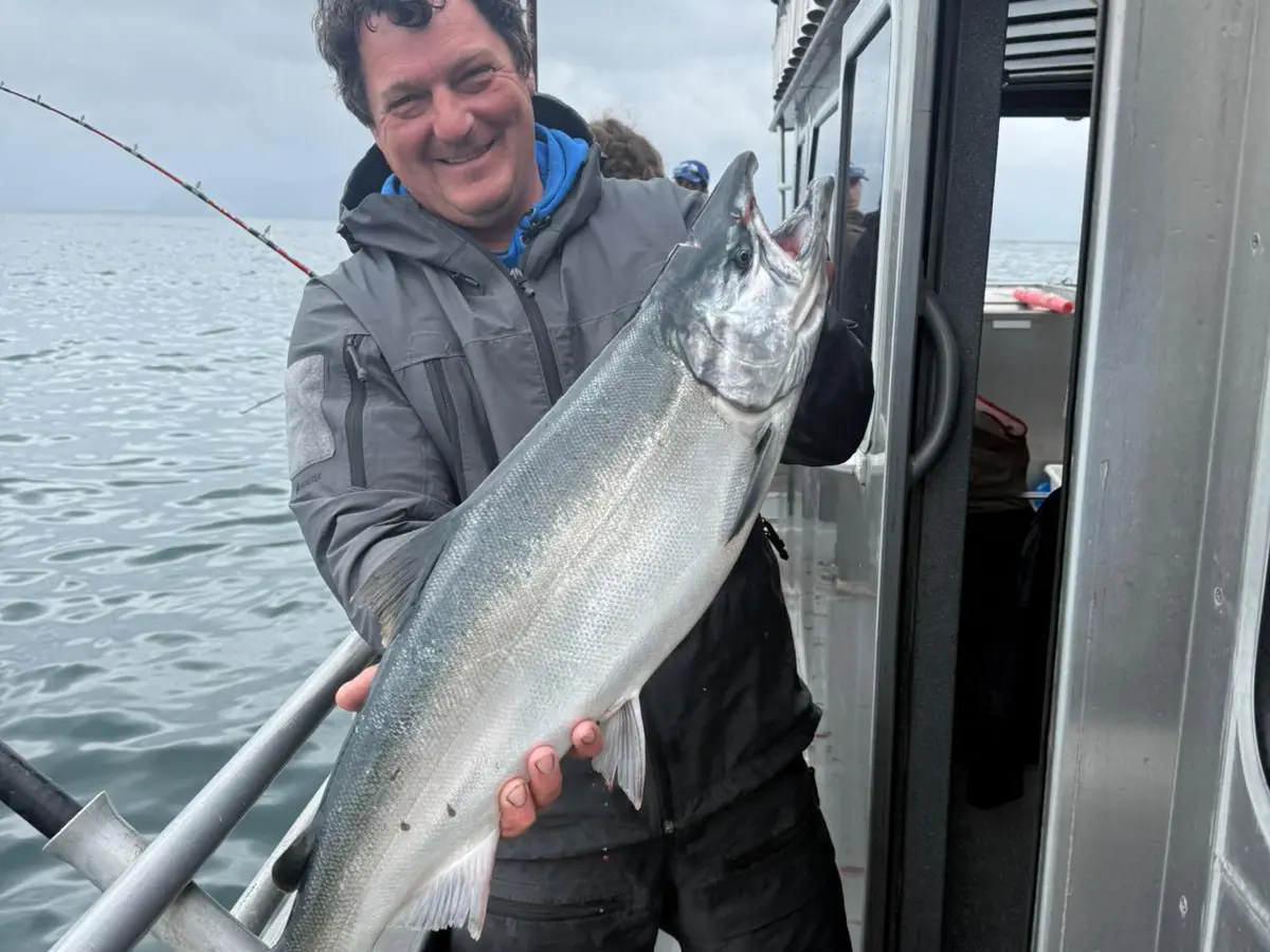 Person holding a large fish on a boat, with a cloudy sky in the background.